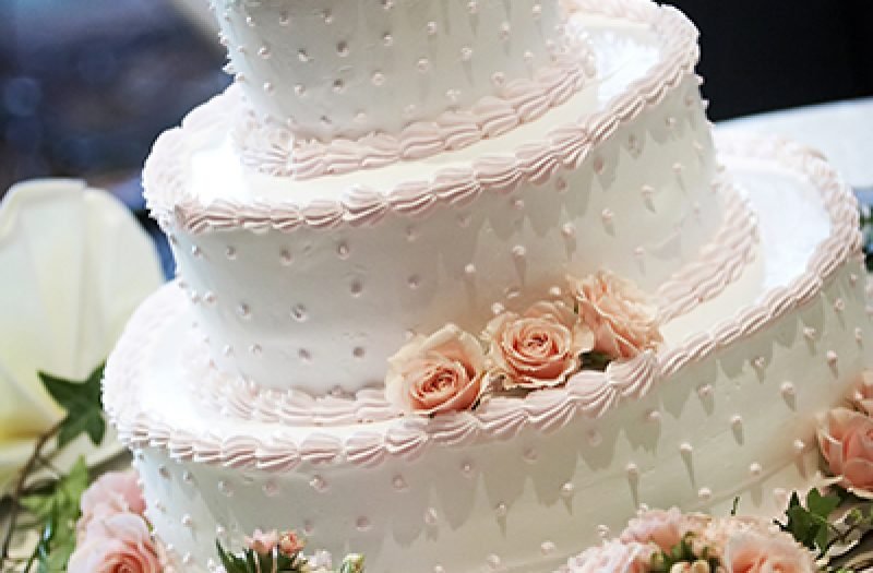 A three tiered wedding cake, shallow depth of field with the focus on the center of the cake. Pink roses on top.